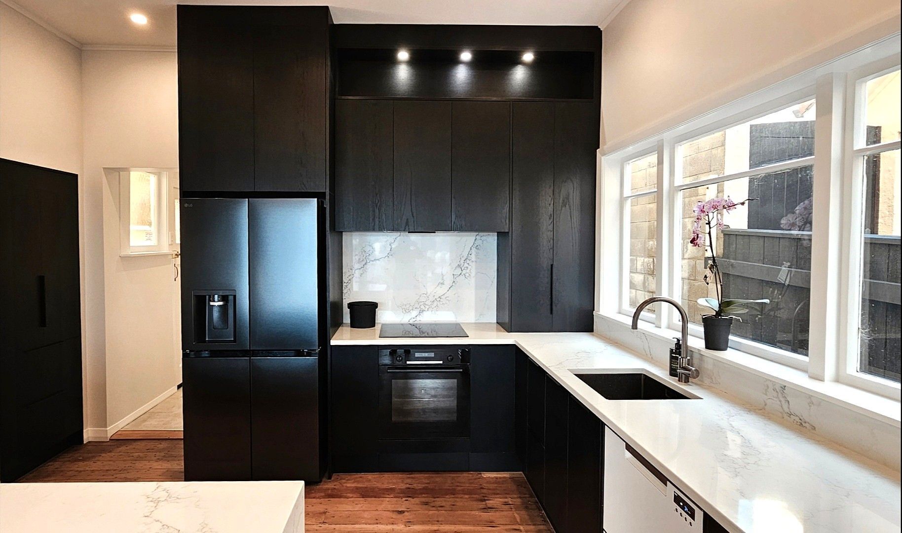 A kitchen with black cabinets , a stainless steel refrigerator , a sink , and a window.