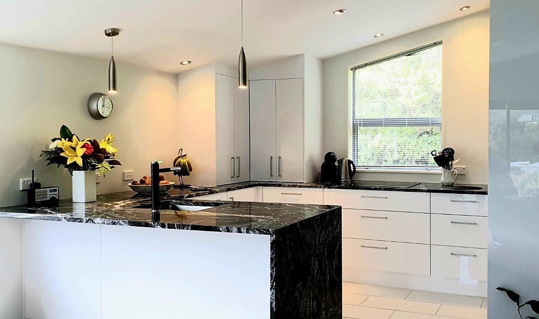 A kitchen with white cabinets , granite counter tops , a sink and a window.