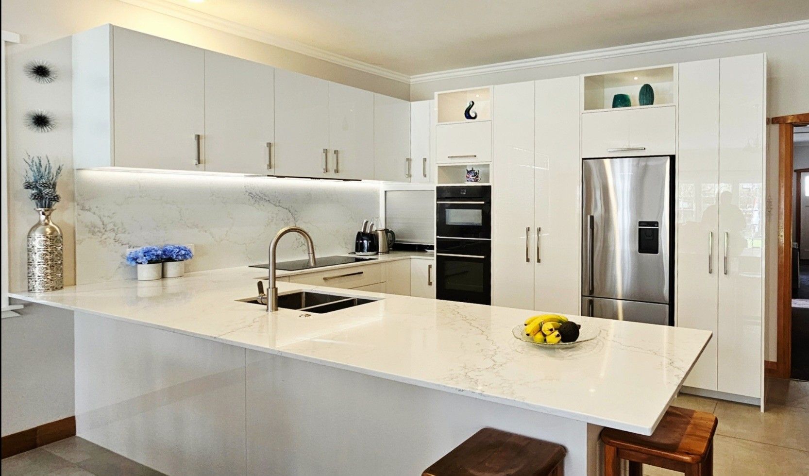 A kitchen with white cabinets , a stainless steel refrigerator , a sink , and a large island.