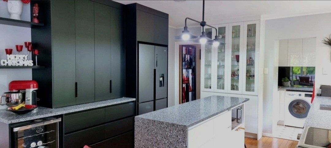A kitchen with black cabinets , granite counter tops , a refrigerator and a washing machine.