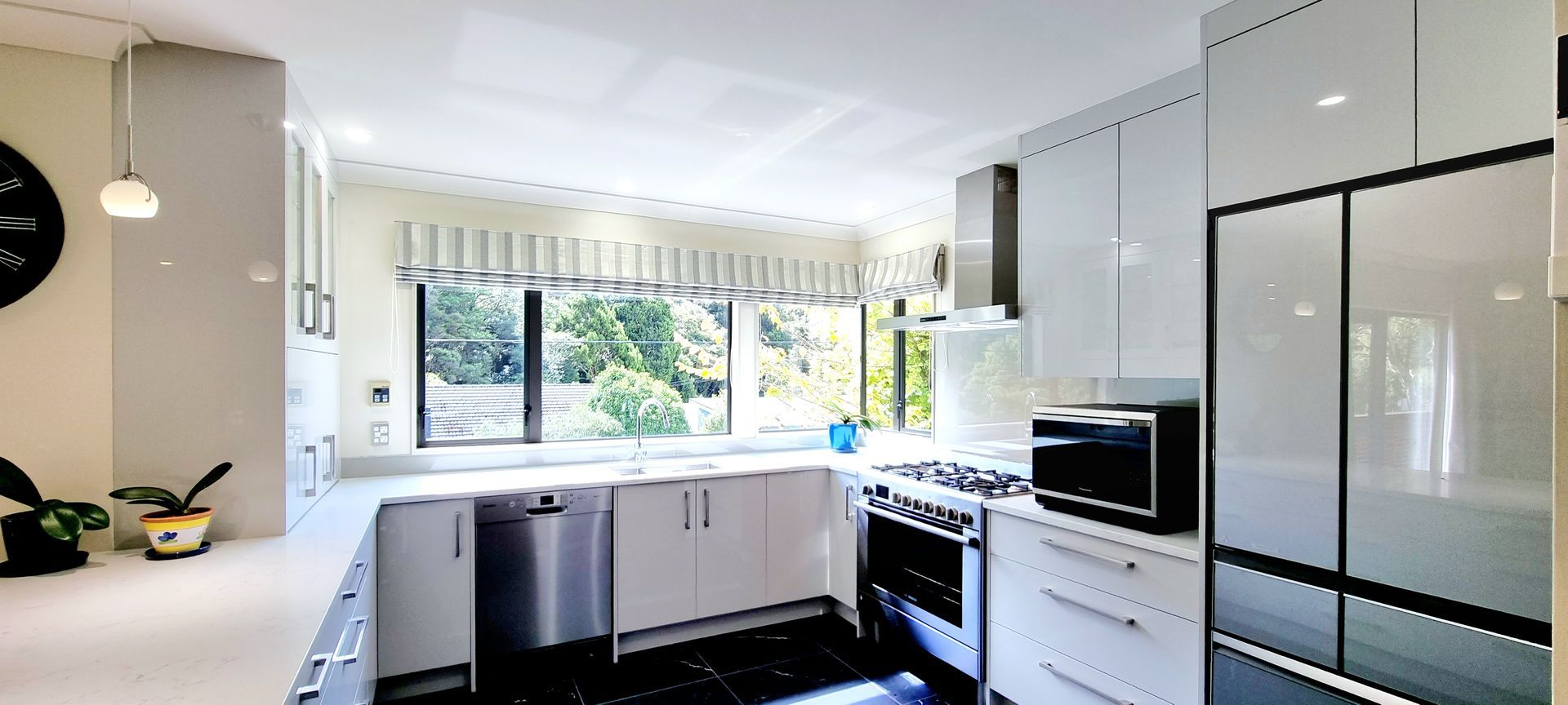 A kitchen with white cabinets , black counter tops , stainless steel appliances and a clock on the wall.
