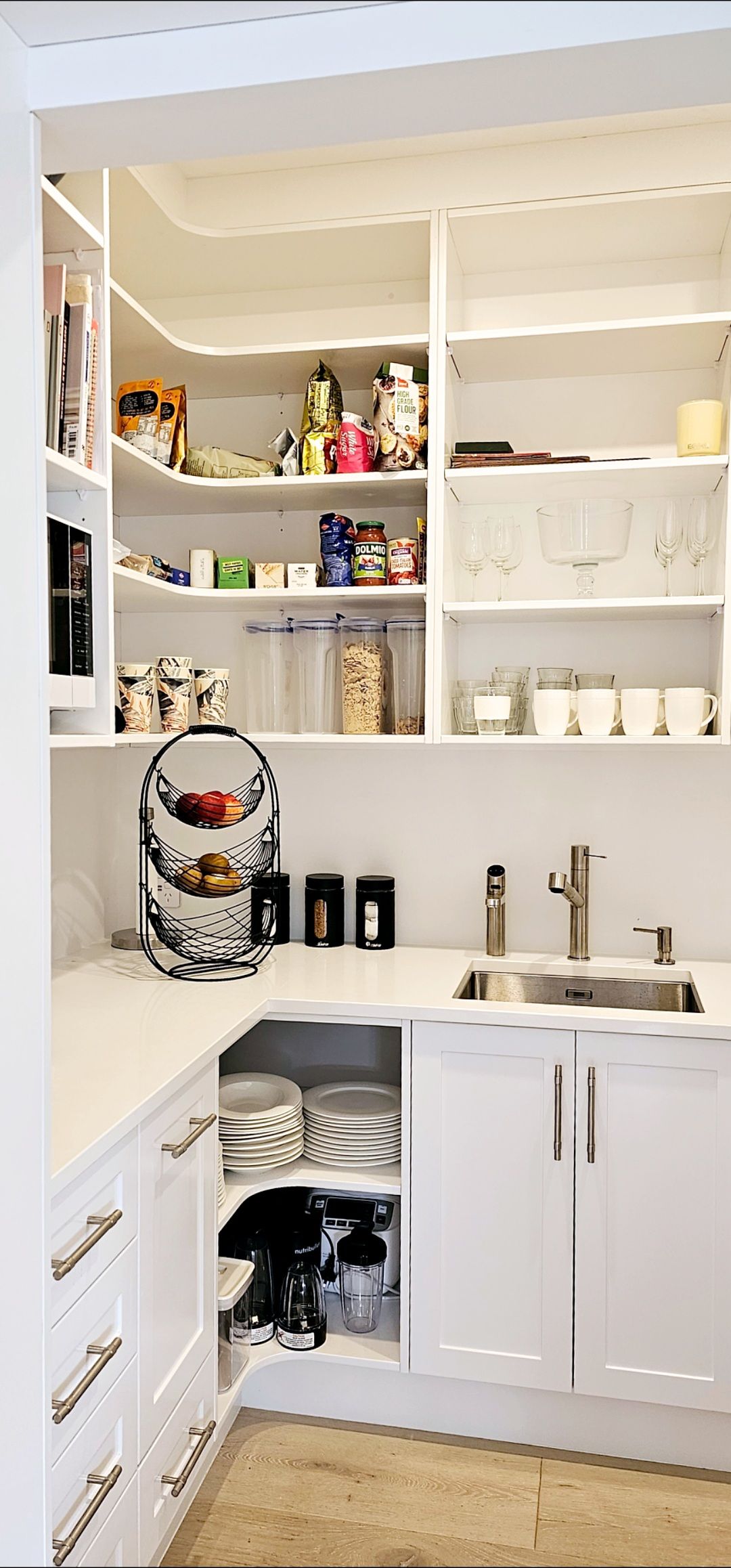 A kitchen with white cabinets , a sink , and shelves.