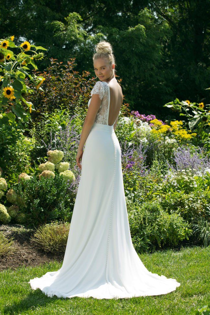 Eine Frau in einem weißen Hochzeitskleid steht in einem Garten.