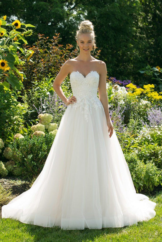 Eine Frau in einem weißen Hochzeitskleid steht in einem Garten.