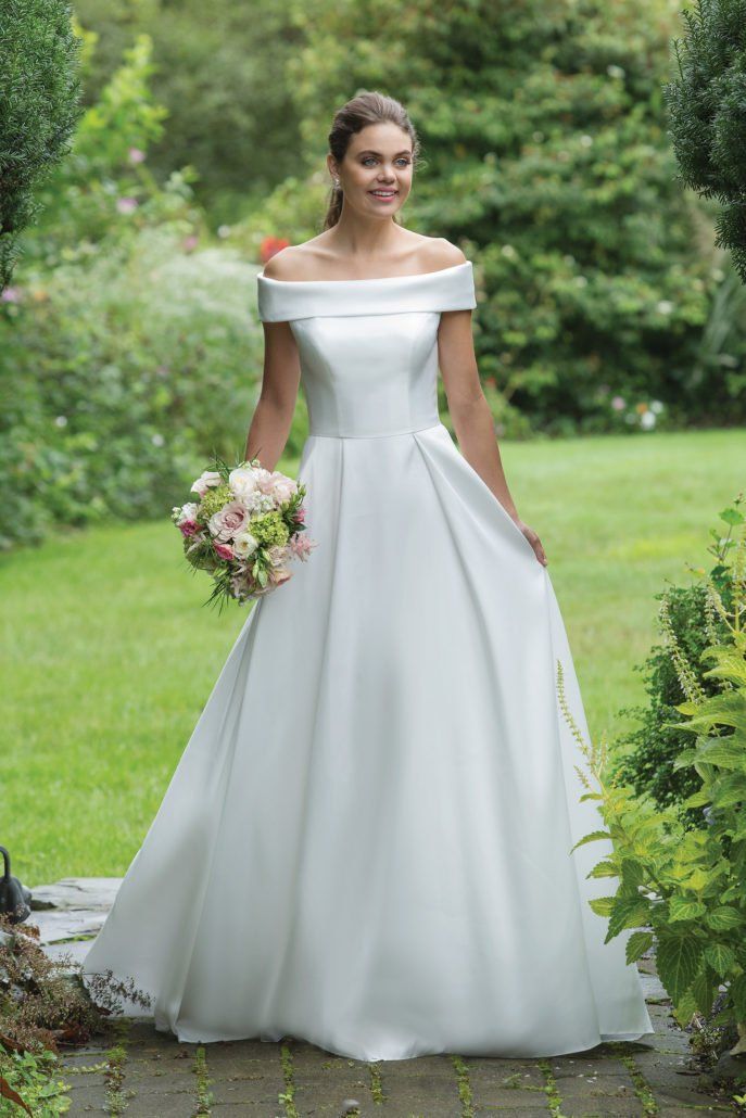Eine Frau in einem weißen Hochzeitskleid hält einen Blumenstrauß.