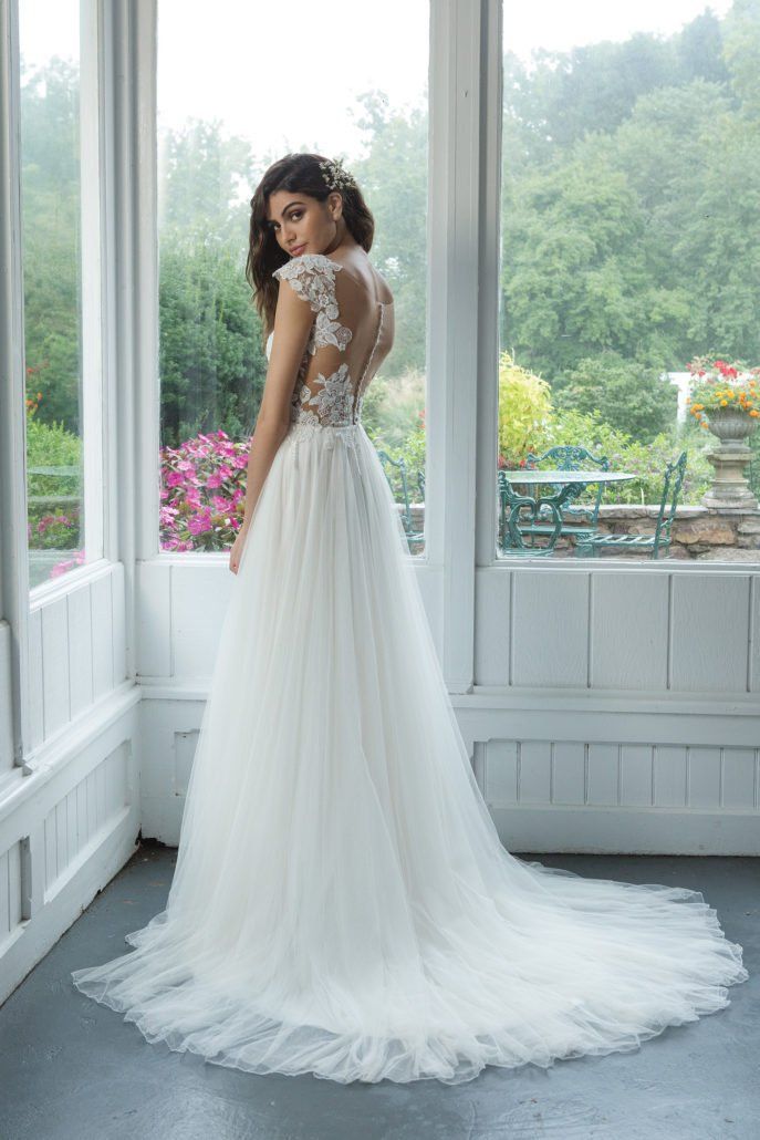 Eine Frau in einem weißen Brautkleid steht vor einem Fenster.