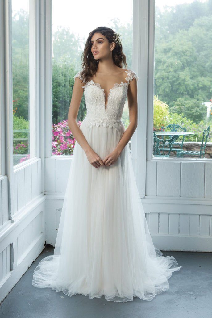 Eine Frau in einem weißen Brautkleid steht vor einem Fenster.