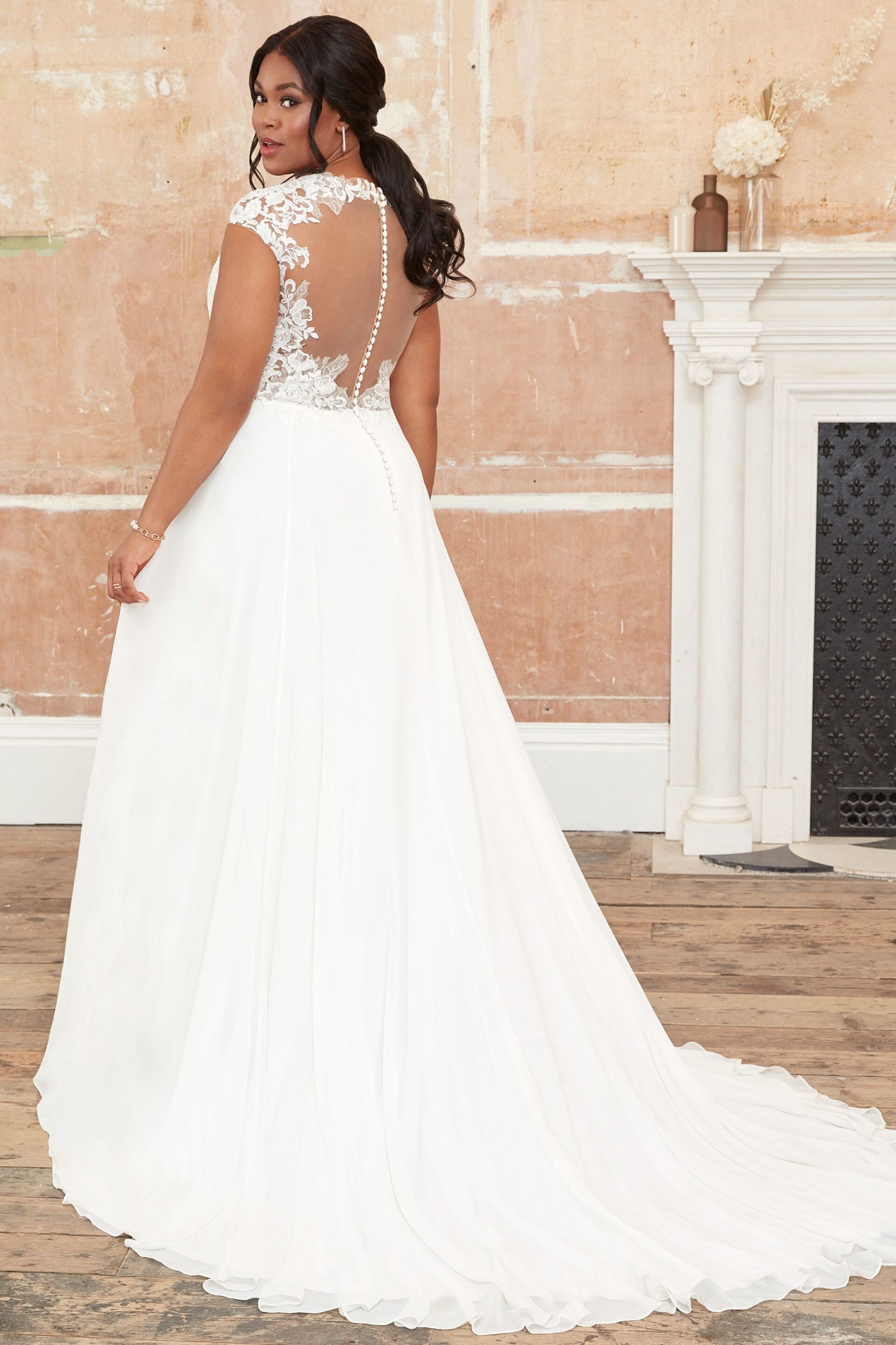 Eine Frau in einem weißen Hochzeitskleid steht vor einem Kamin.