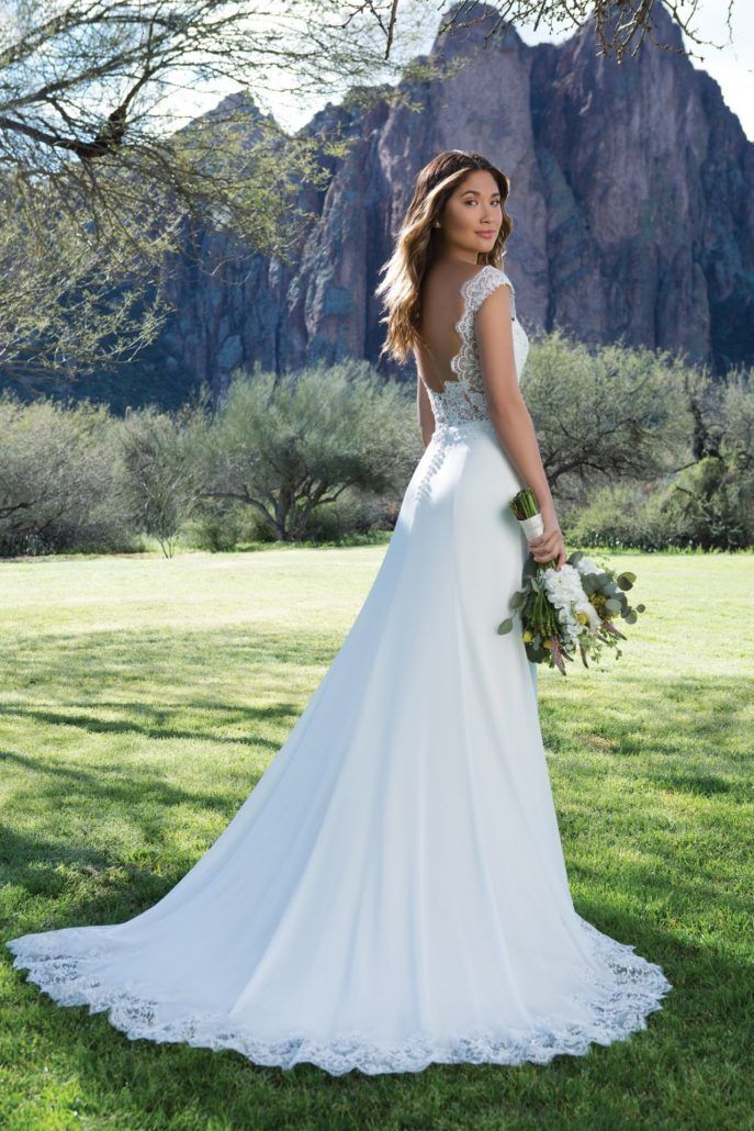 Eine Frau in einem weißen Hochzeitskleid steht auf einem Feld und hält einen Blumenstrauß in der Hand.