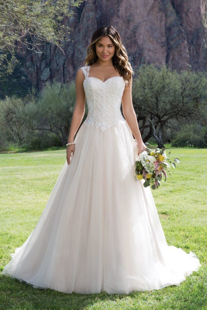 Eine Frau in einem weißen Brautkleid steht im Gras und hält einen Blumenstrauß in der Hand.