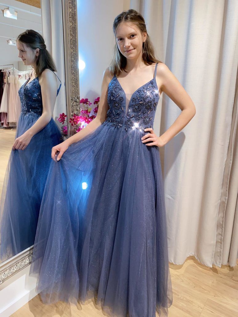 Eine Frau in einem blauen Kleid steht vor einem Spiegel.