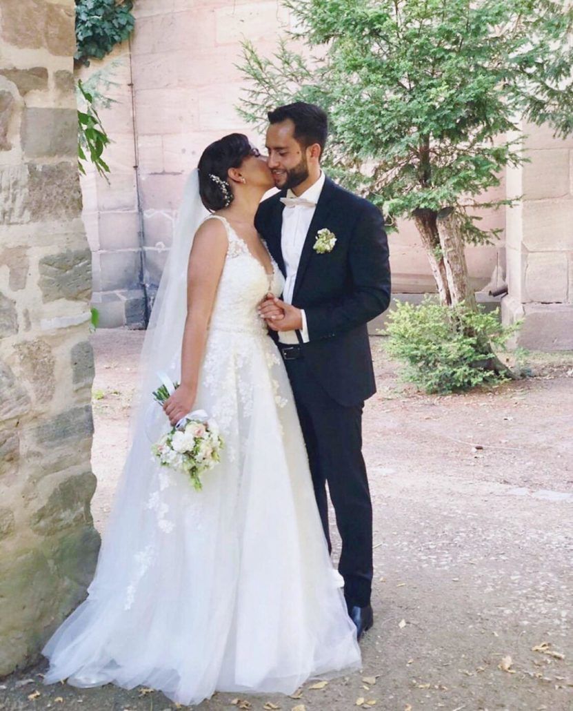 Braut und Bräutigam küssen sich vor einer Steinmauer