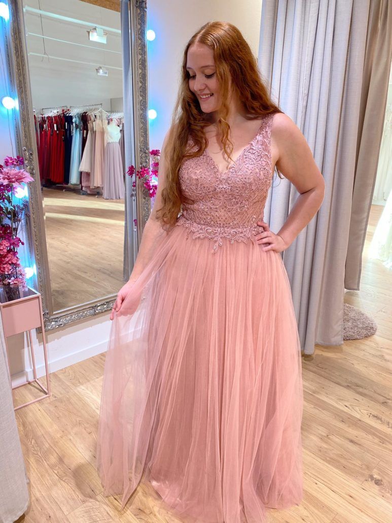 Eine Frau in einem rosa Kleid steht vor einem Spiegel.