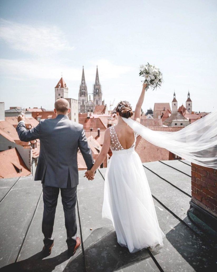 Eine Braut und ein Bräutigam stehen auf einem Dach und halten sich an den Händen.