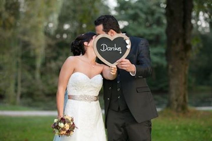 Eine Braut und ein Bräutigam küssen sich hinter einem Schild mit der Aufschrift „Danke“