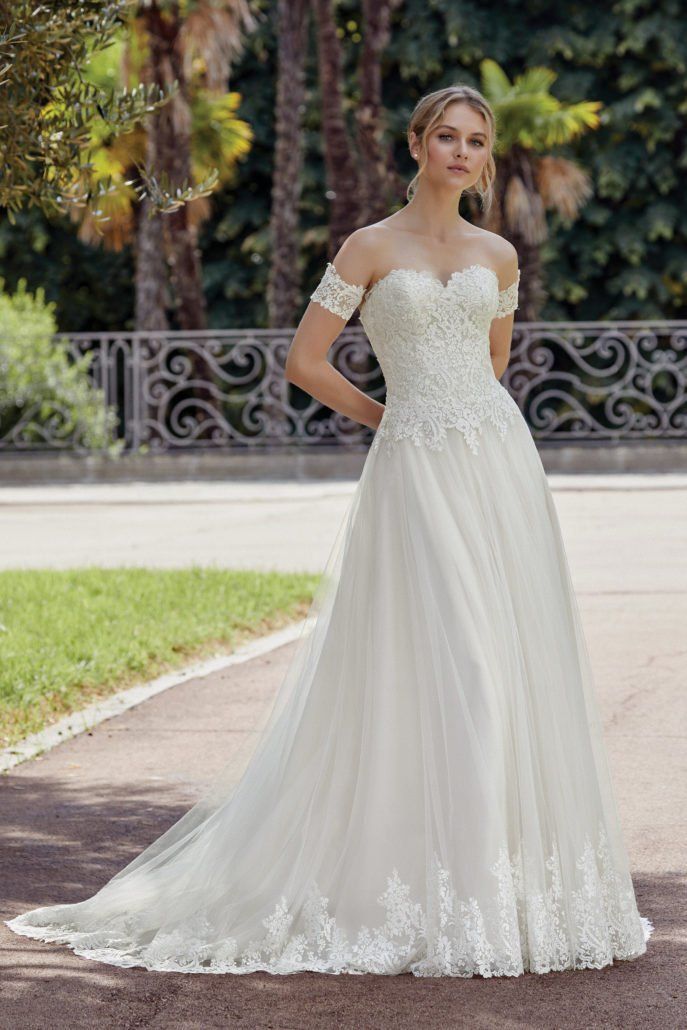 Eine Frau in einem weißen Brautkleid steht vor einem Zaun.