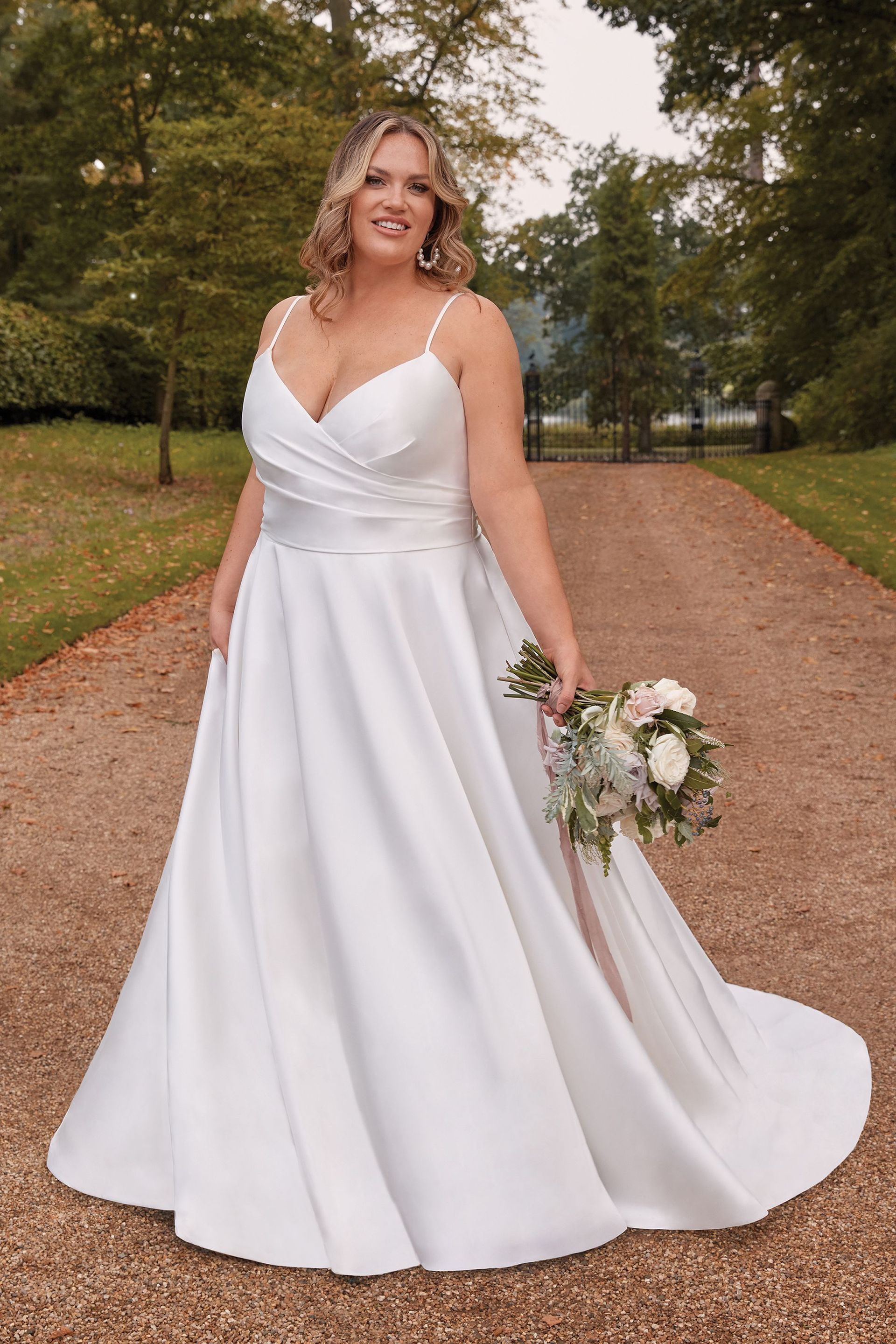 Eine Übergrößenbraut in einem weißen Brautkleid hält einen Blumenstrauß.