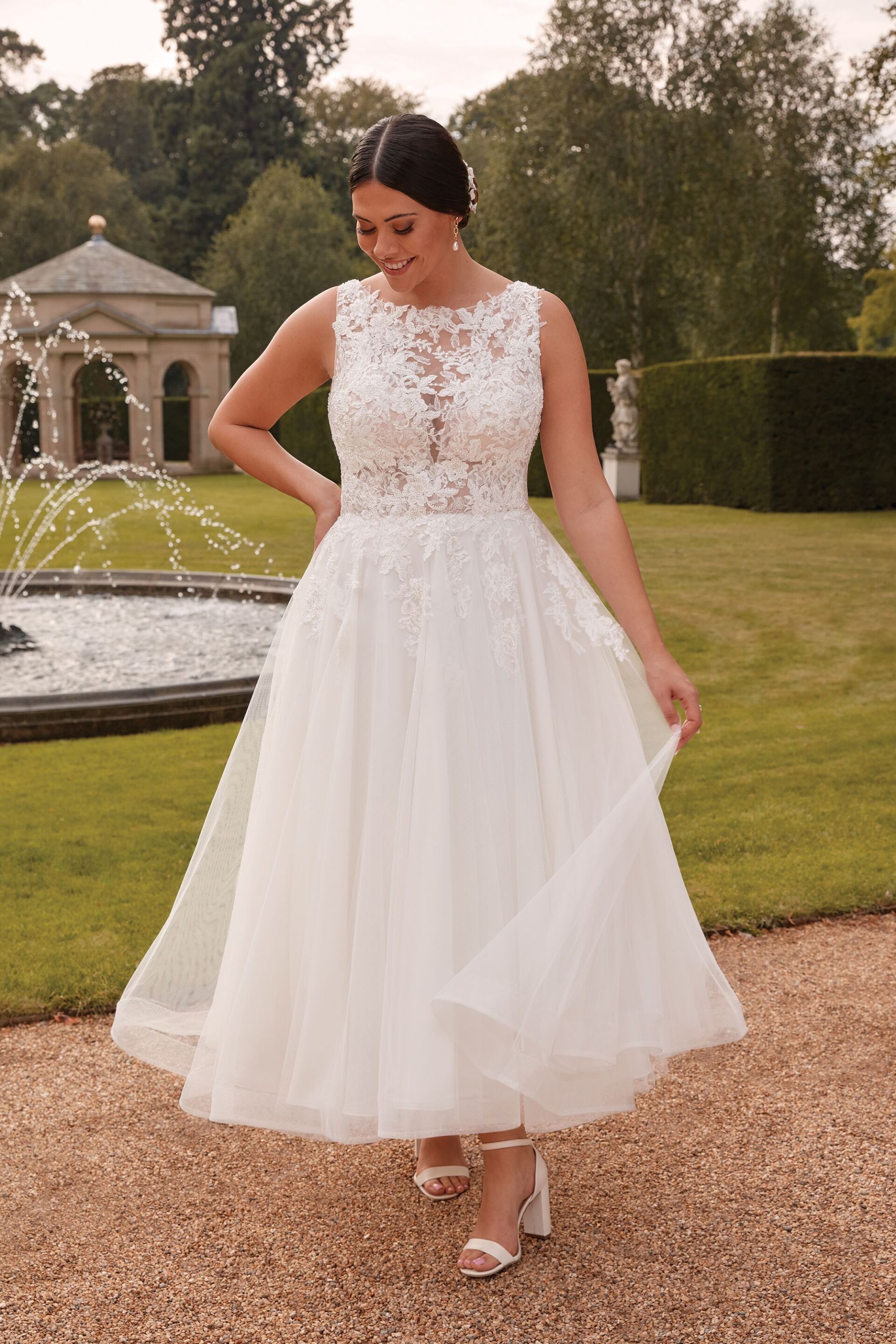 Eine Frau in einem weißen Hochzeitskleid steht vor einem Brunnen.