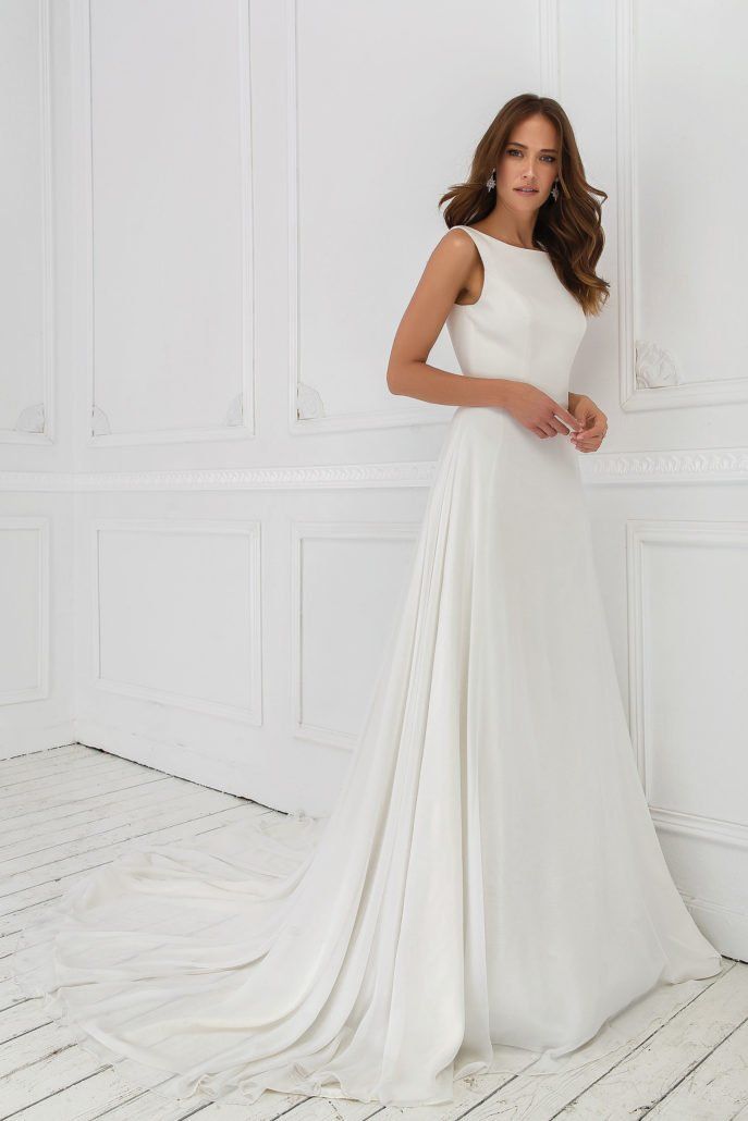 Eine Frau in einem weißen Brautkleid steht vor einer weißen Wand.