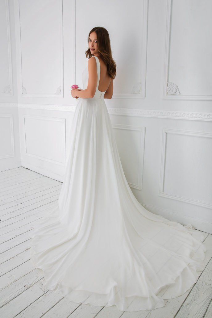 Eine Frau in einem weißen Brautkleid steht vor einer weißen Wand.