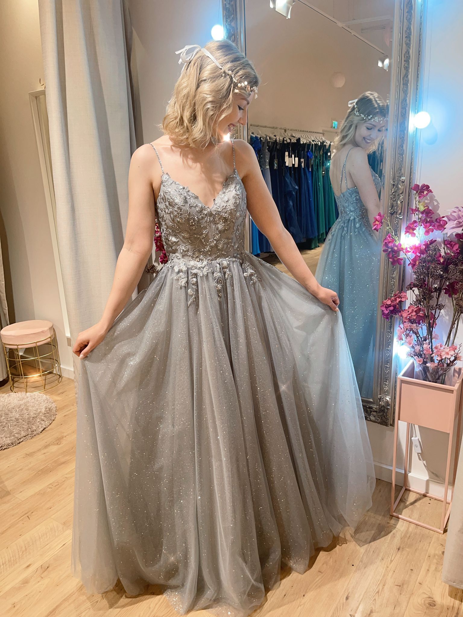 Eine Frau in einem langen silbernen Kleid steht vor einem Spiegel.