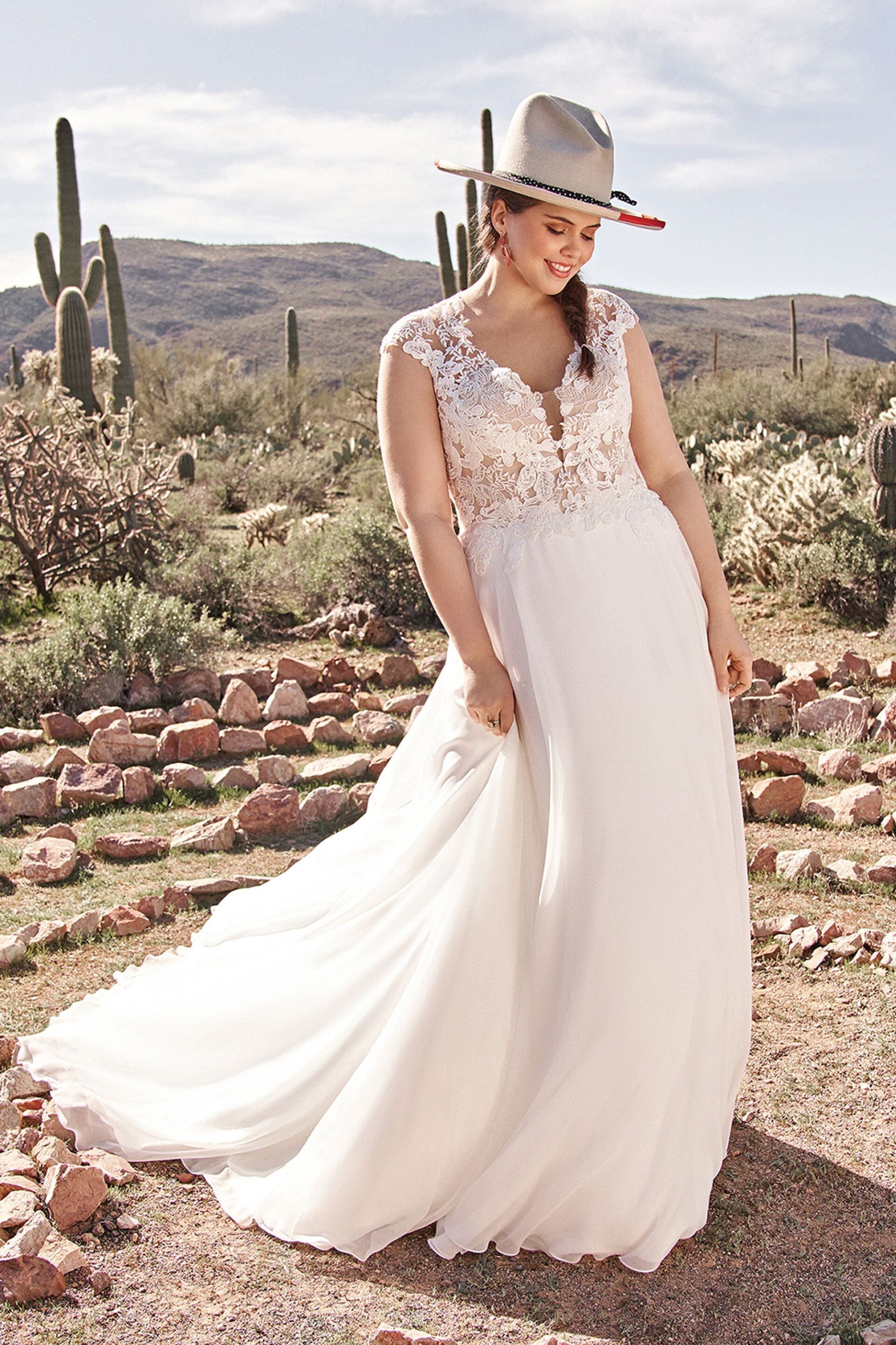 Eine Frau in einem Hochzeitskleid und Hut steht in der Wüste.