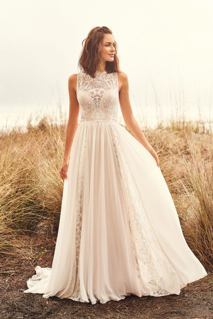 Eine Frau in einem weißen Hochzeitskleid steht auf einem Feld.