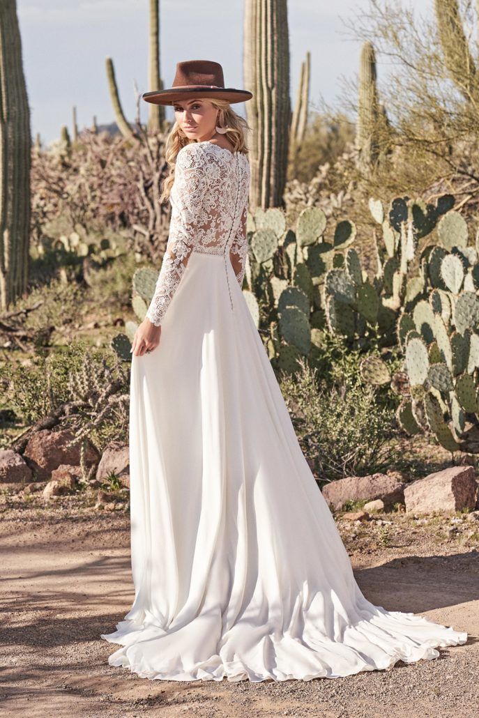 Eine Frau trägt in der Wüste ein weißes Hochzeitskleid und einen Hut.