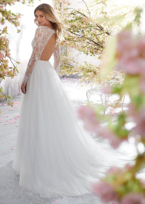 Eine Frau trägt ein weißes Hochzeitskleid mit langen Ärmeln und tiefem Rückenausschnitt.