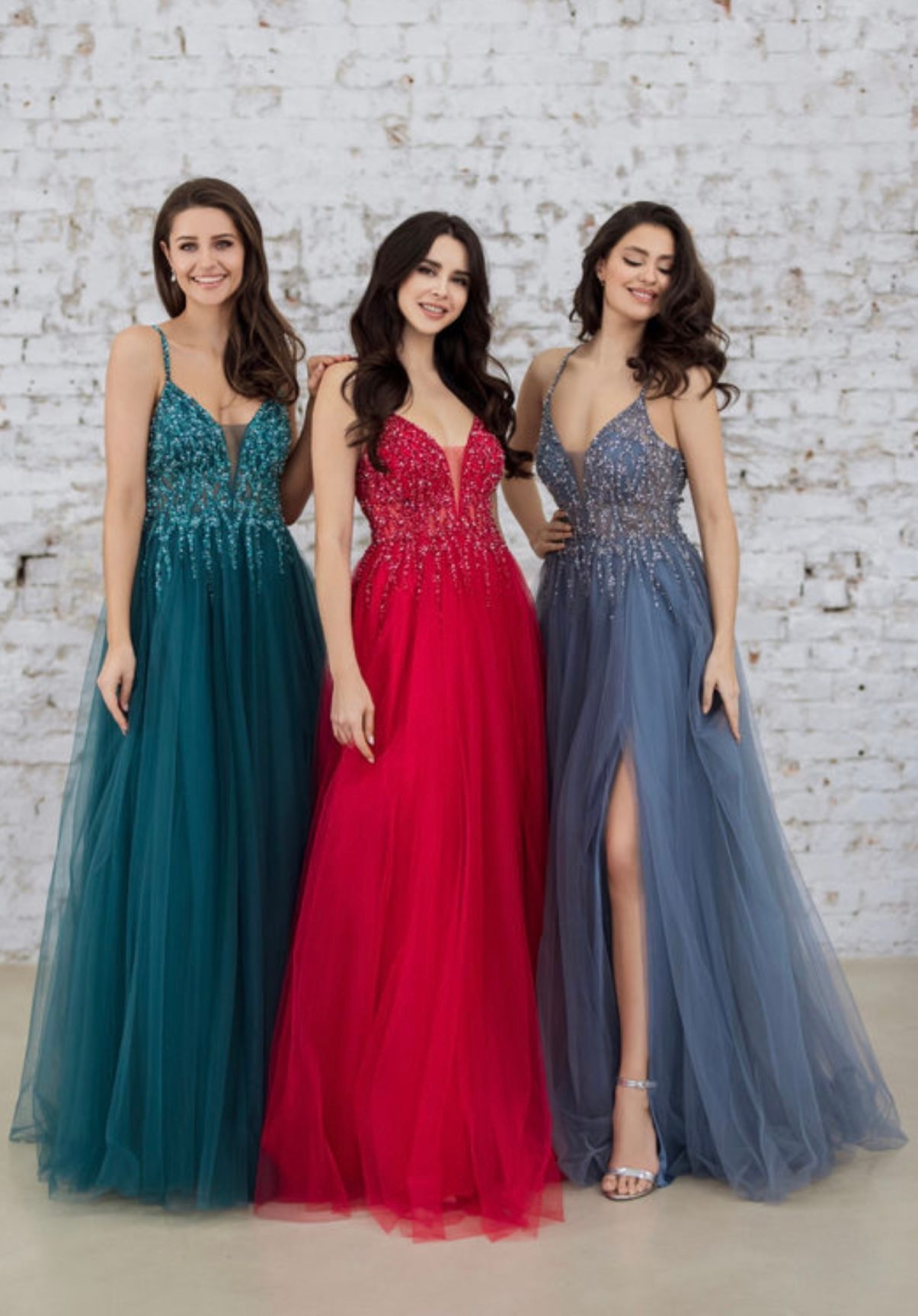 Drei Frauen in langen Kleidern stehen nebeneinander vor einer Backsteinmauer.