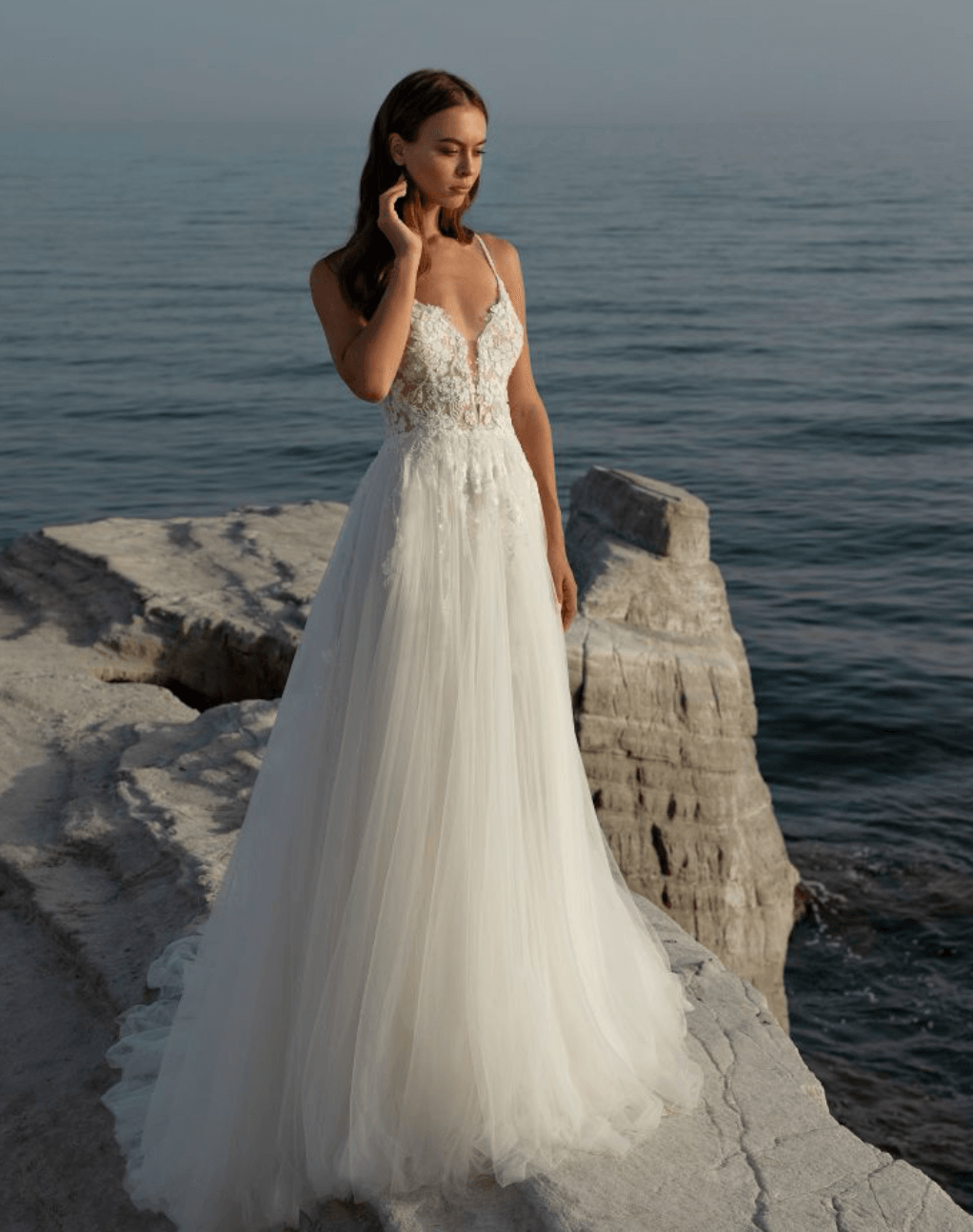 Eine Frau in einem weißen Hochzeitskleid steht auf einem Felsen in der Nähe des Meeres.