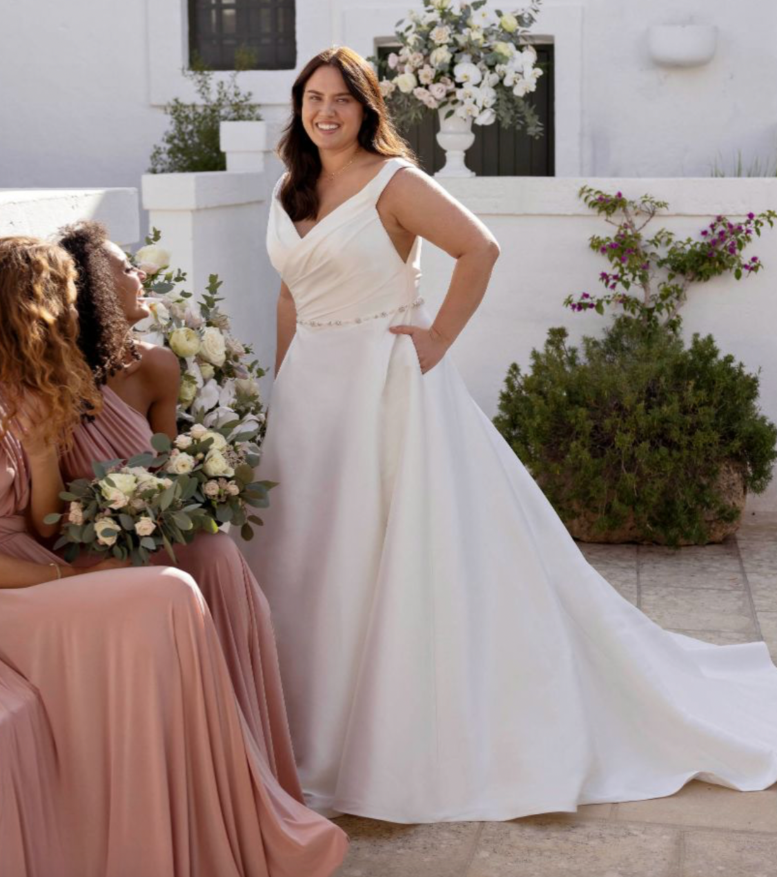 Eine Frau in einem weißen Kleid steht neben zwei Frauen in rosa Kleidern