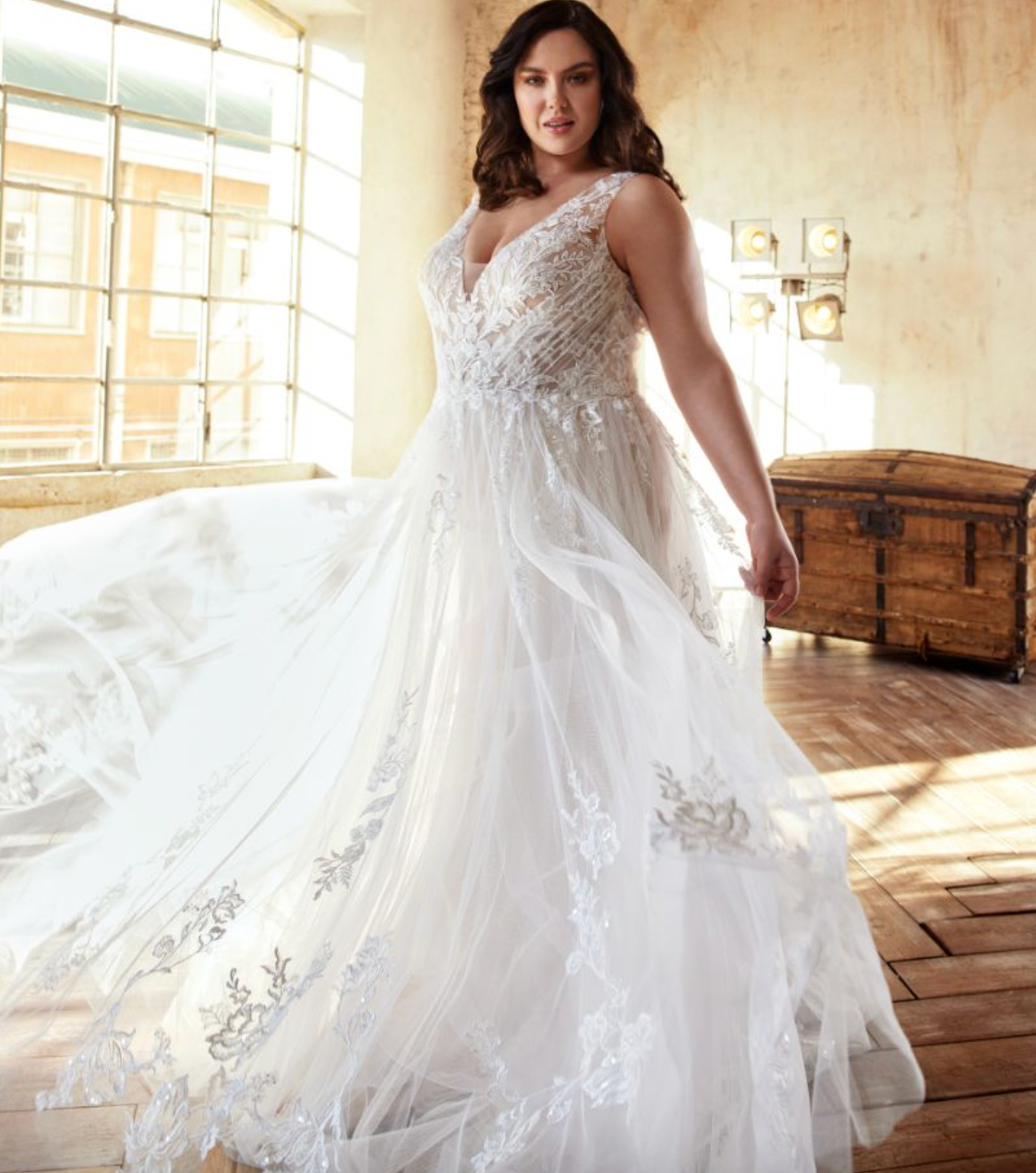 Eine Frau in einem weißen Brautkleid steht vor einem Fenster.