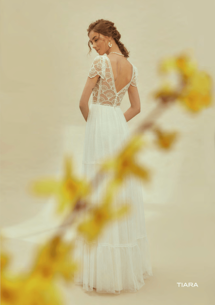 Eine Frau in einem weißen Hochzeitskleid steht vor einer gelben Blume.