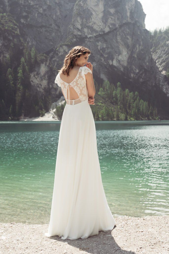 Eine Frau in einem weißen Hochzeitskleid steht neben einem See.