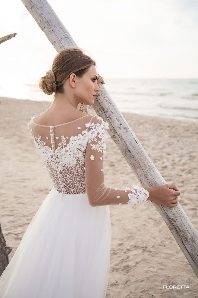 Eine Frau in einem Brautkleid steht an einem Strand und hält eine Stange.