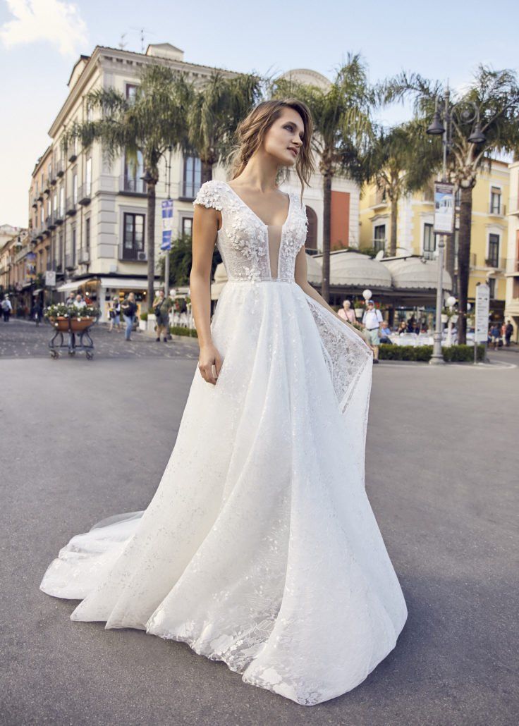 Eine Frau in einem weißen Brautkleid steht auf einer Straße vor einem Gebäude.