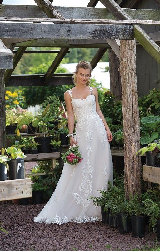 Eine Frau im Brautkleid steht in einem Gewächshaus und hält einen Blumenstrauß in der Hand.
