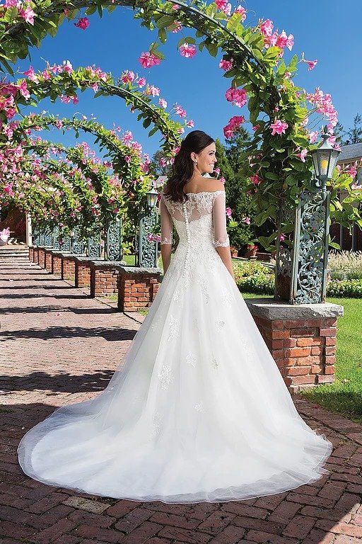 Eine Frau in einem weißen Hochzeitskleid steht vor Blumen.