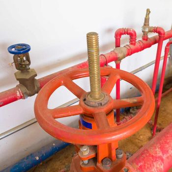 Red industrial valve with a large wheel on red pipes.