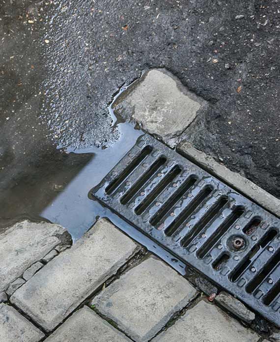 Wet asphalt and brick with water pooling near a black storm drain.