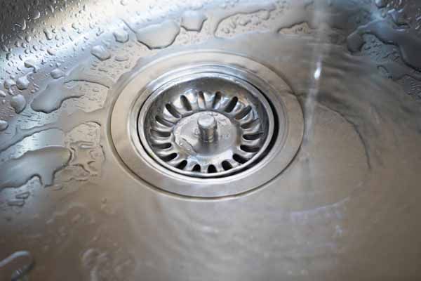 Stainless steel sink with water draining, focus on the drain.