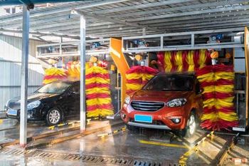 Two cars being washed at a car wash with yellow, red, and orange brushes.