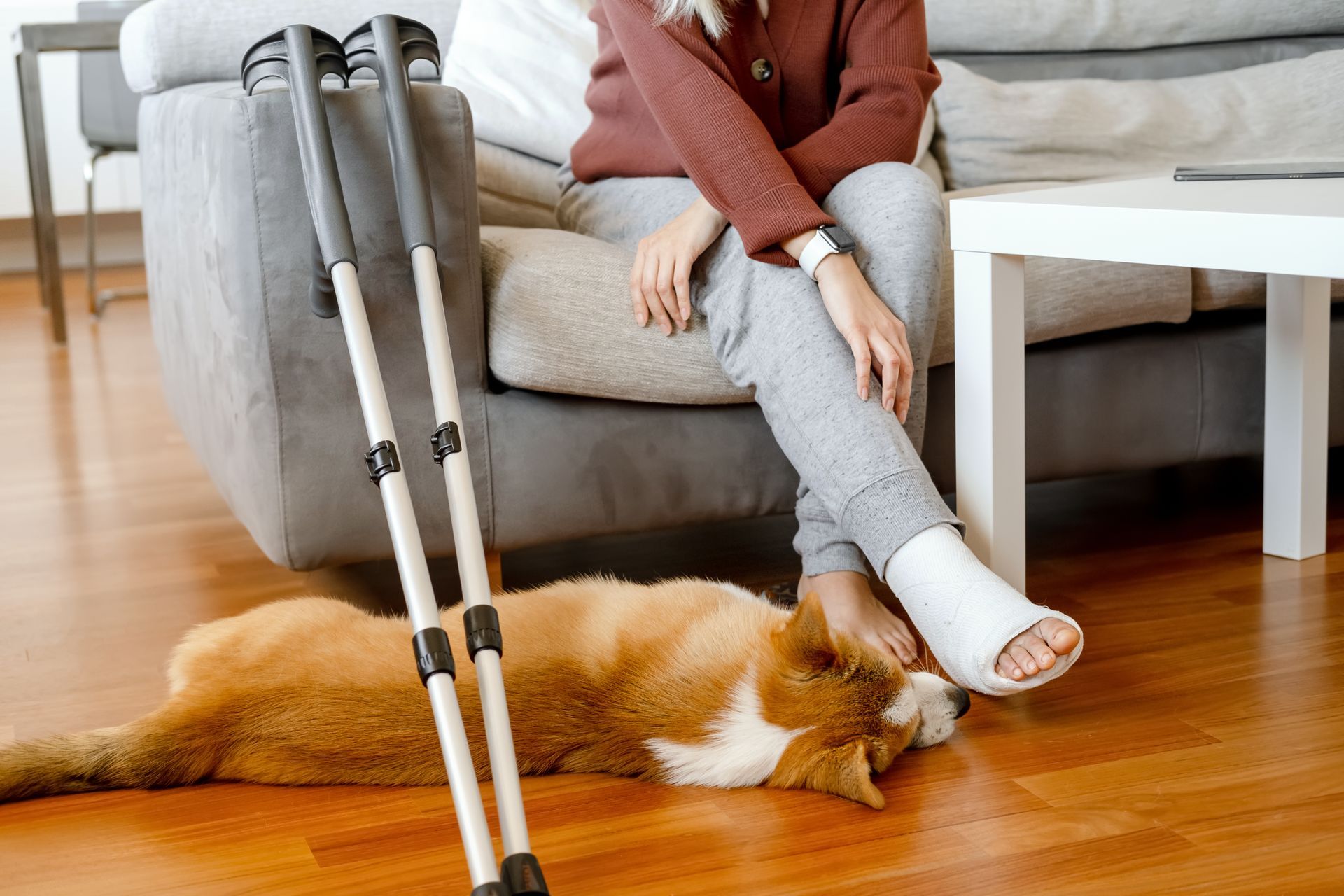 The same young woman sits, her face out of frame, with the corgy laying by her feet - they are both relaxed because they have employee disability insurance