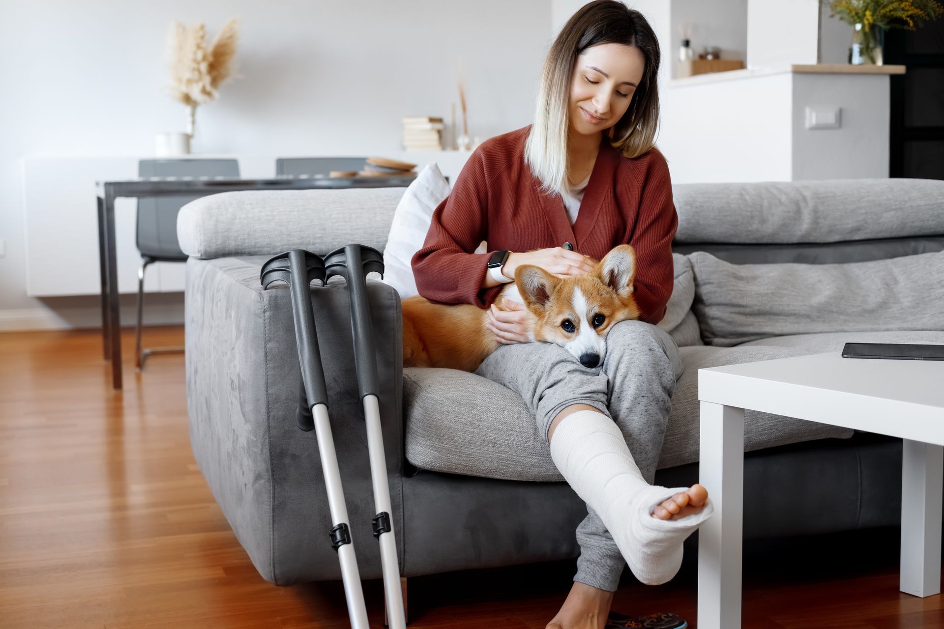 A young woman in a leg cast holds a corgi dog in her lap - she knows the difference between short term vs long term disability