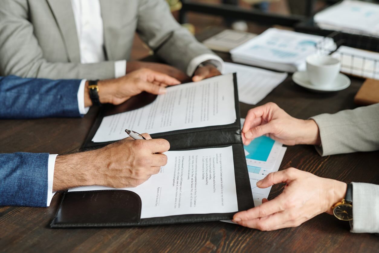 Three businesspeople discuss a contract while one person signs the document.