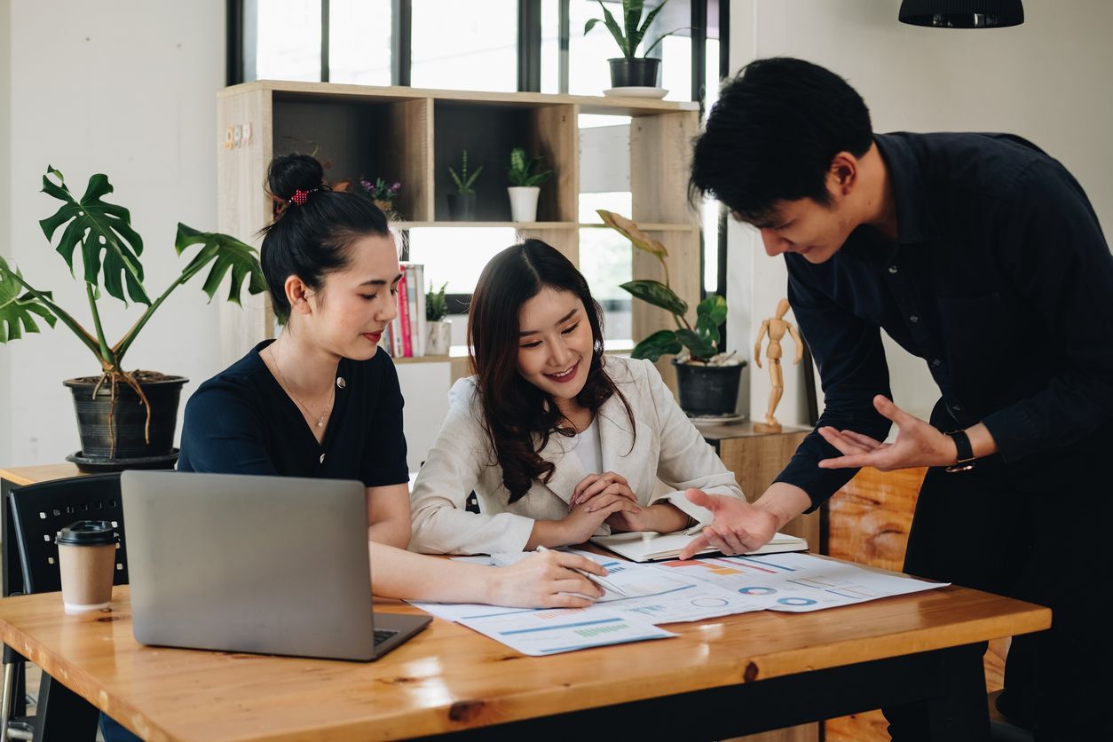 Three people sit around a table with an open laptop and several business documents.