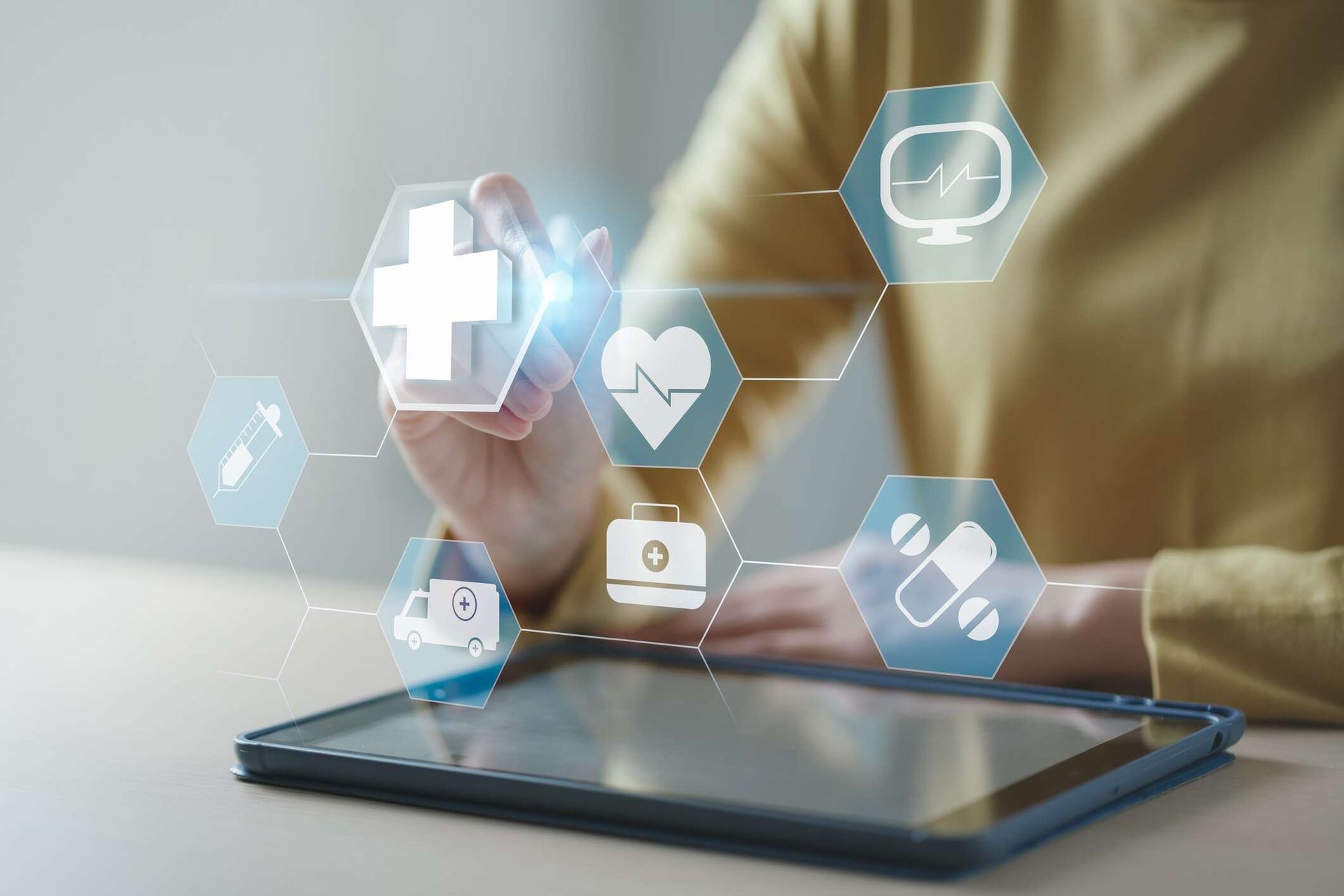 A person wearing a yellow long-sleeved shirt selects a healthcare icon with a stylus. Six healthcare-themed icons hover over a tablet.