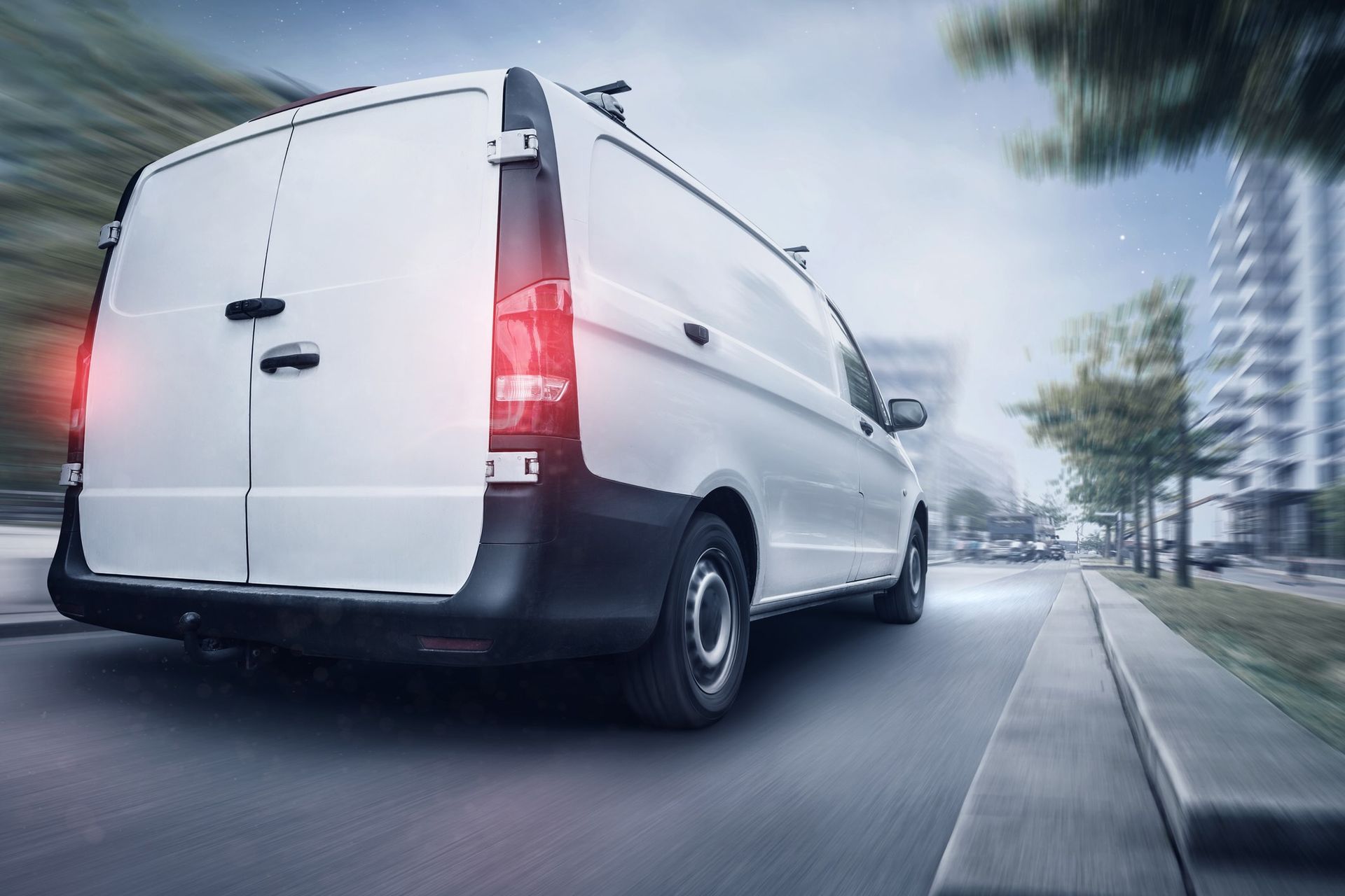 Back view of a white commercial van driving down a busy city street.