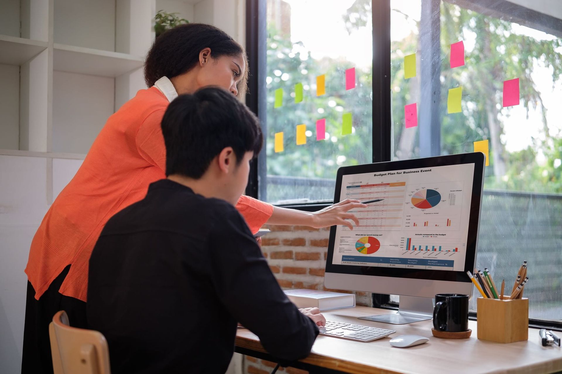 A woman and a man look at analytics on a desktop computer.